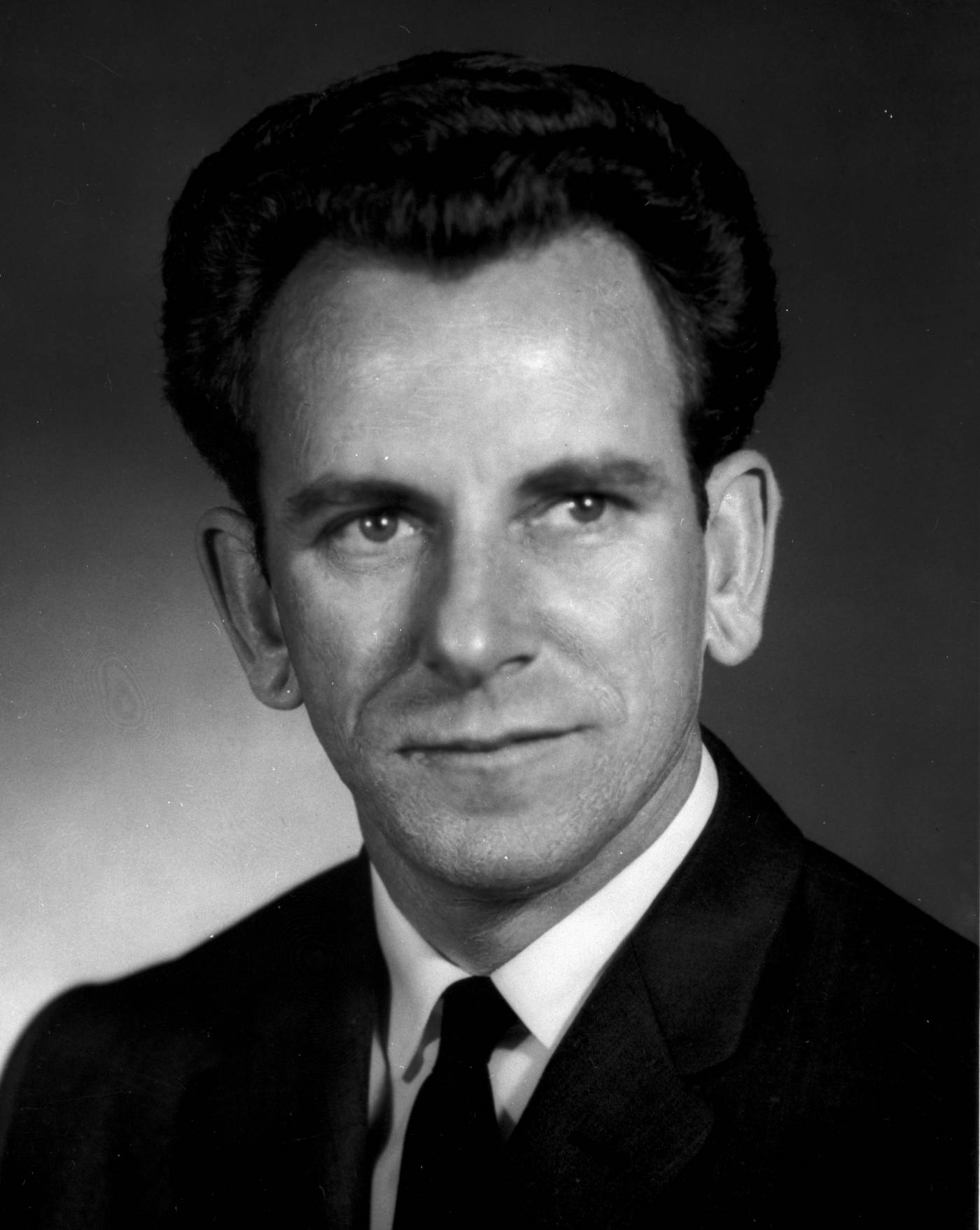 Photographie en noir et blanc, portrait de Germain Bombardier. Il porte un veston, une chemise blanche et une cravate noire.